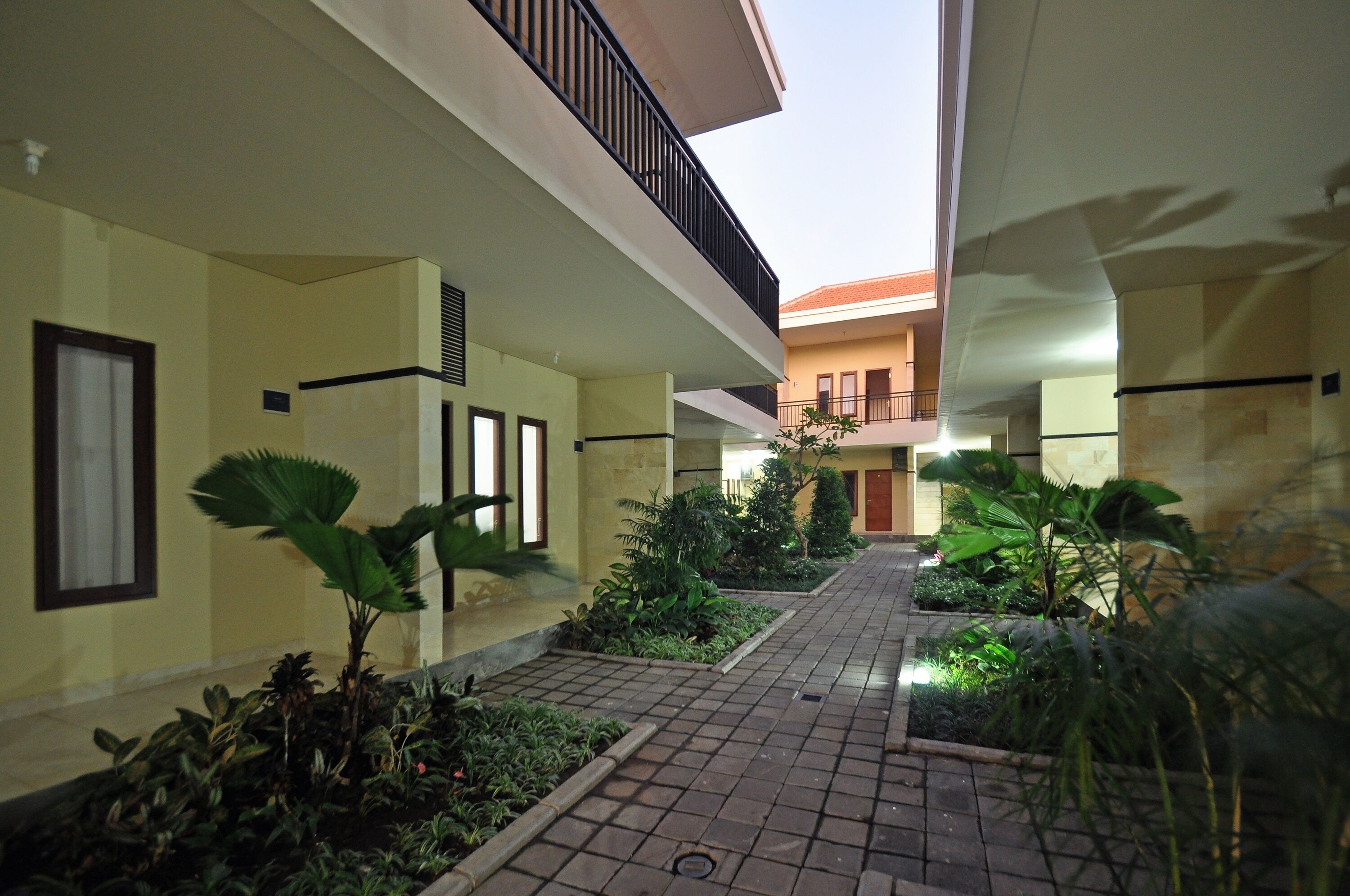 A courtyard with a tiled walkway, potted plants, and a building with balconies.