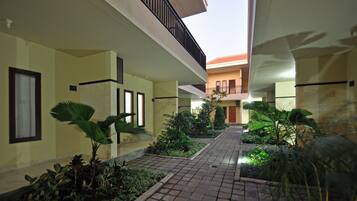 A courtyard with a tiled walkway, potted plants, and a building with balconies.