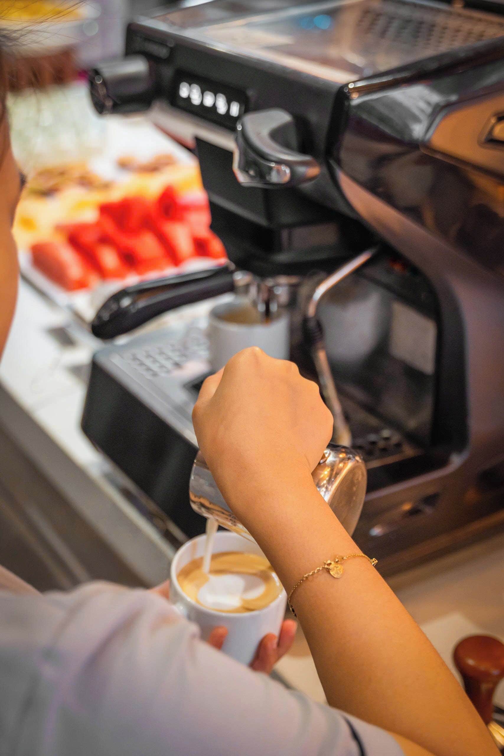 Una persona sosteniendo una taza de café, con una máquina de café al fondo.