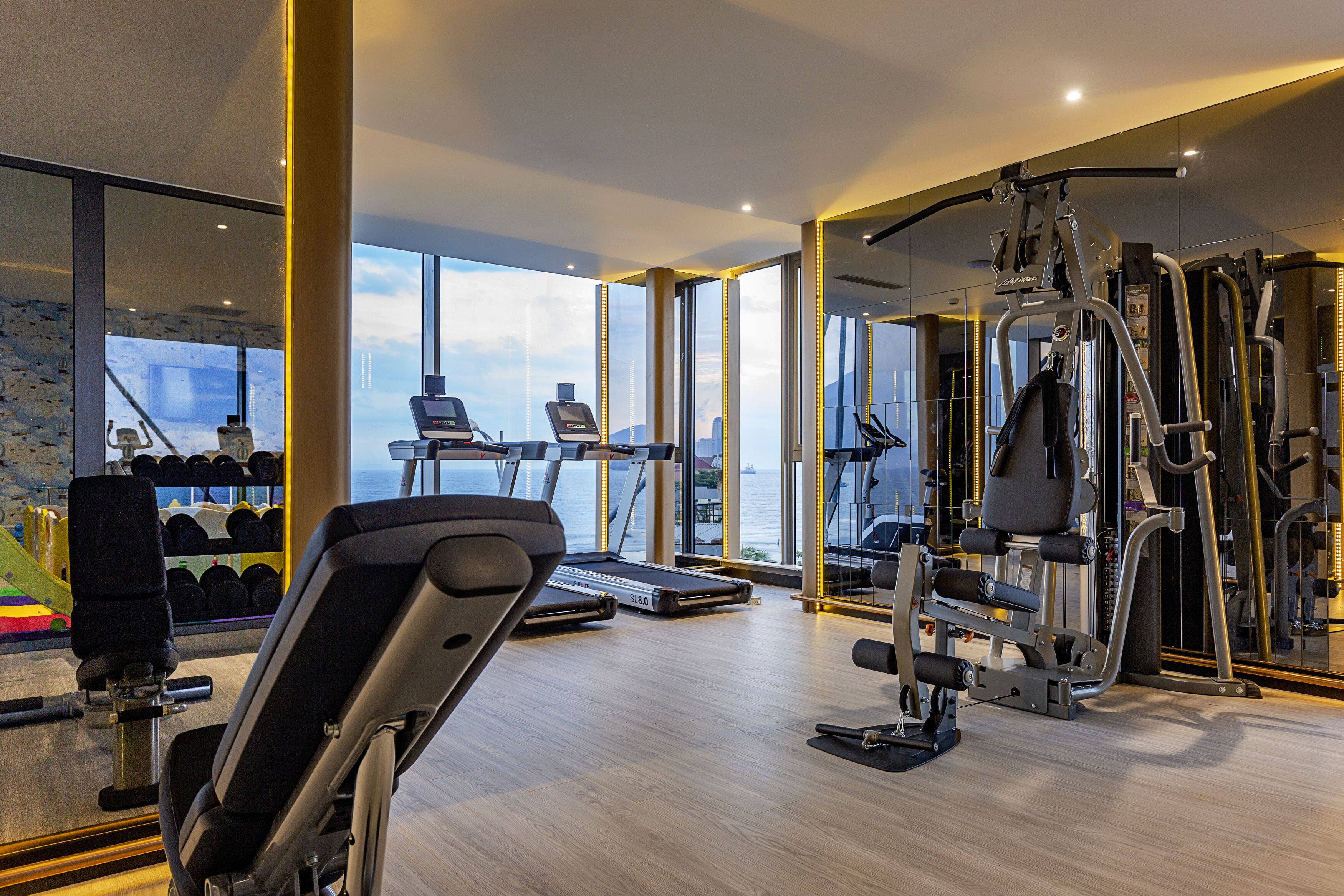 A modern gym with treadmills, weight machines, and a view of the sea.