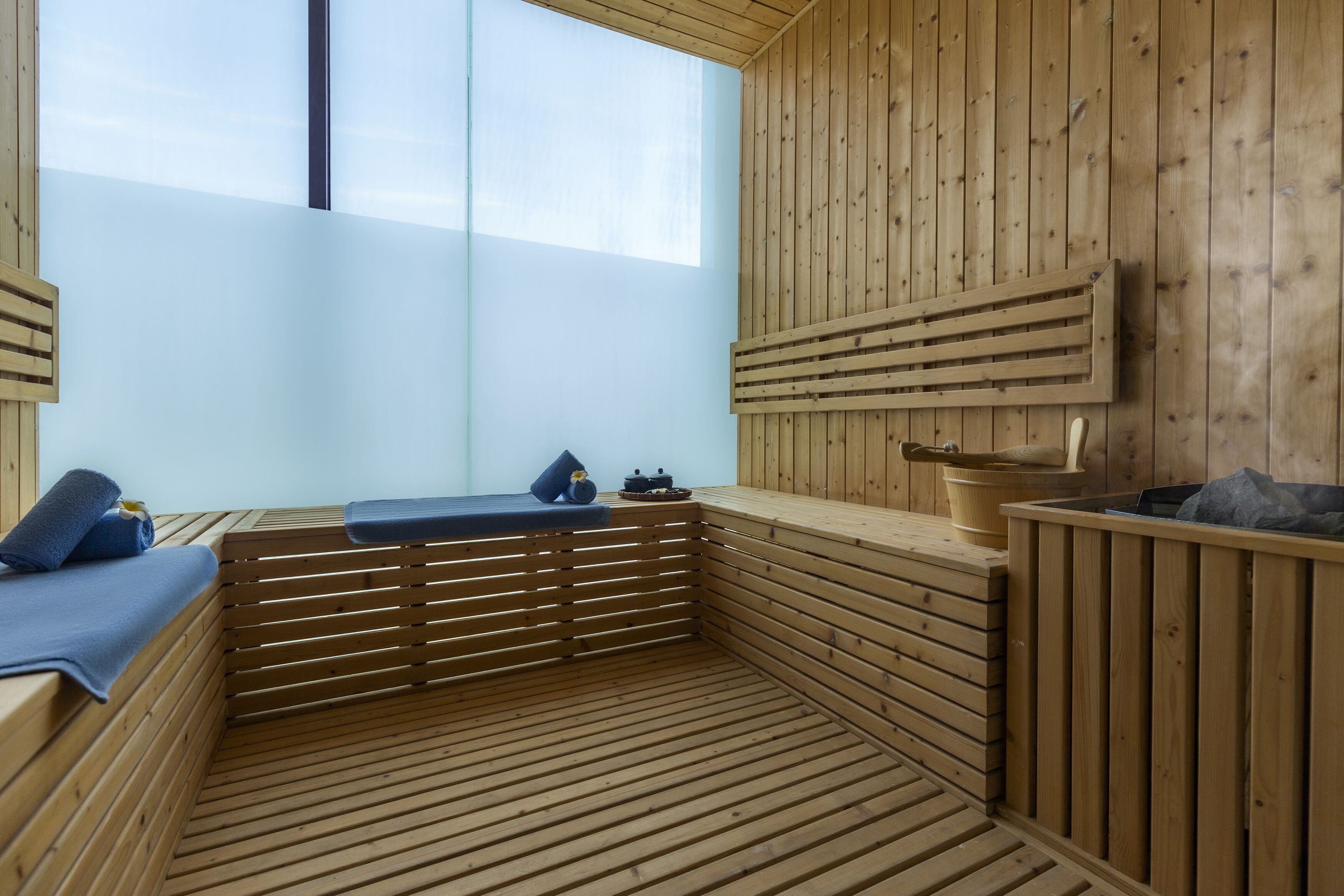 Una sala de sauna con bancos de madera, un banco con una toalla y una pared de madera con una ventana.