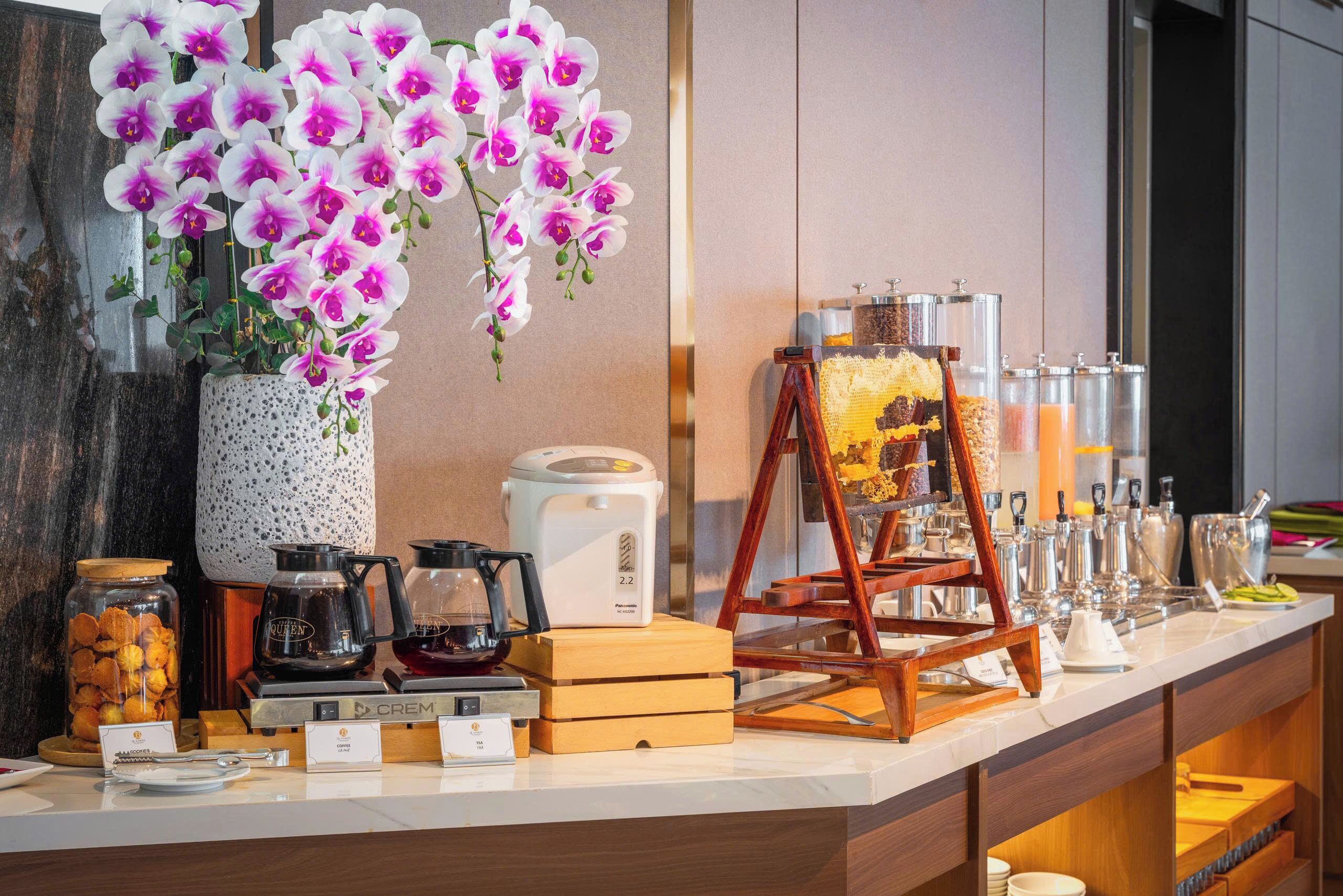 Un espace d’accueil d’hôtel comprenant un coin café, un tableau sur chevalet et un vase rempli d’orchidées.