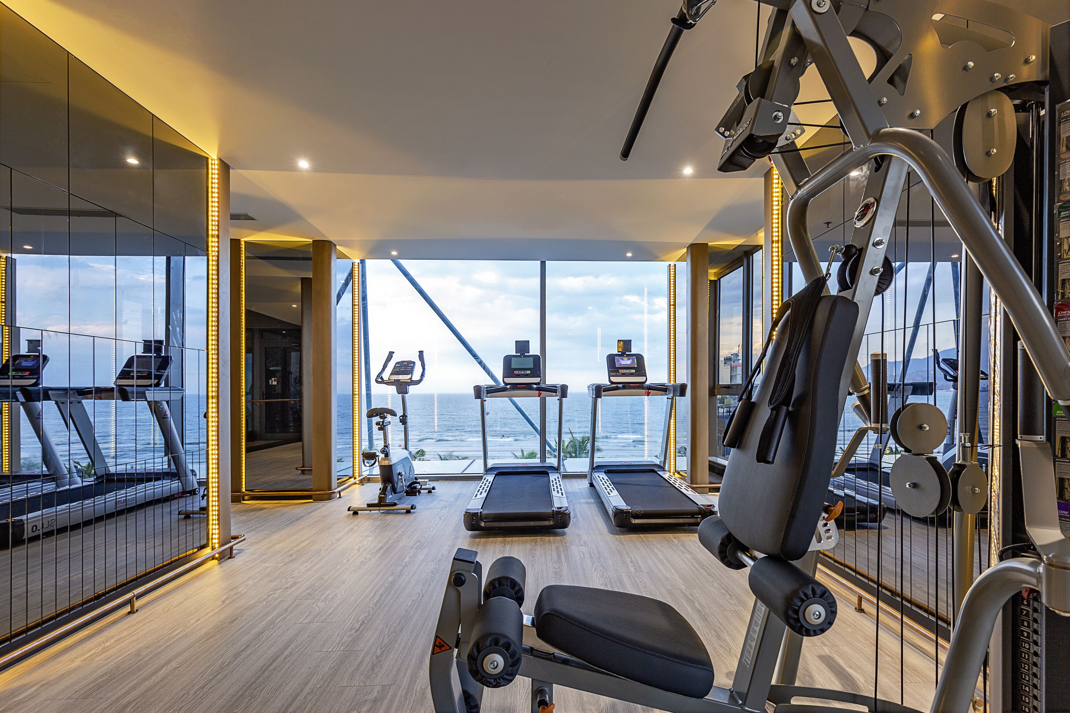 A gym with treadmills, a bench press, and a rowing machine, overlooking a body of water.