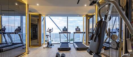 A gym with treadmills, a bench press, and a rowing machine, overlooking a body of water.