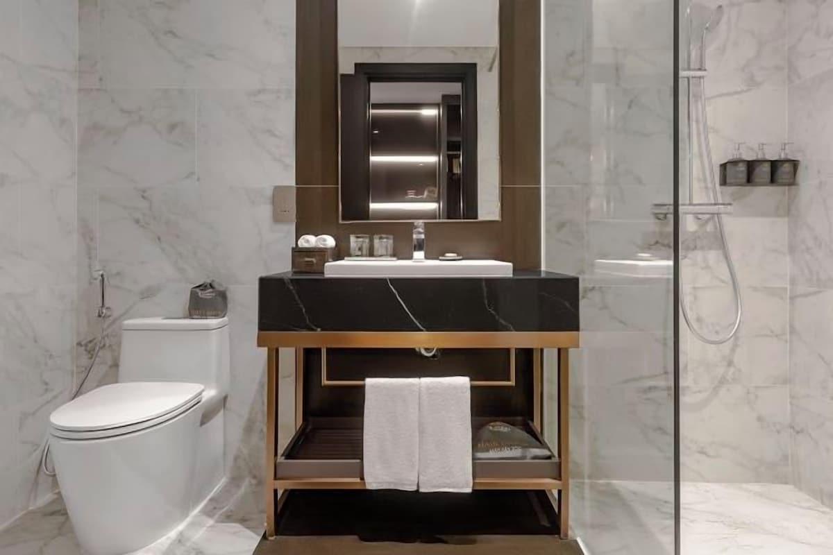 A modern bathroom with a marble floor, a black sink vanity, a toilet, and a glass-enclosed shower area.