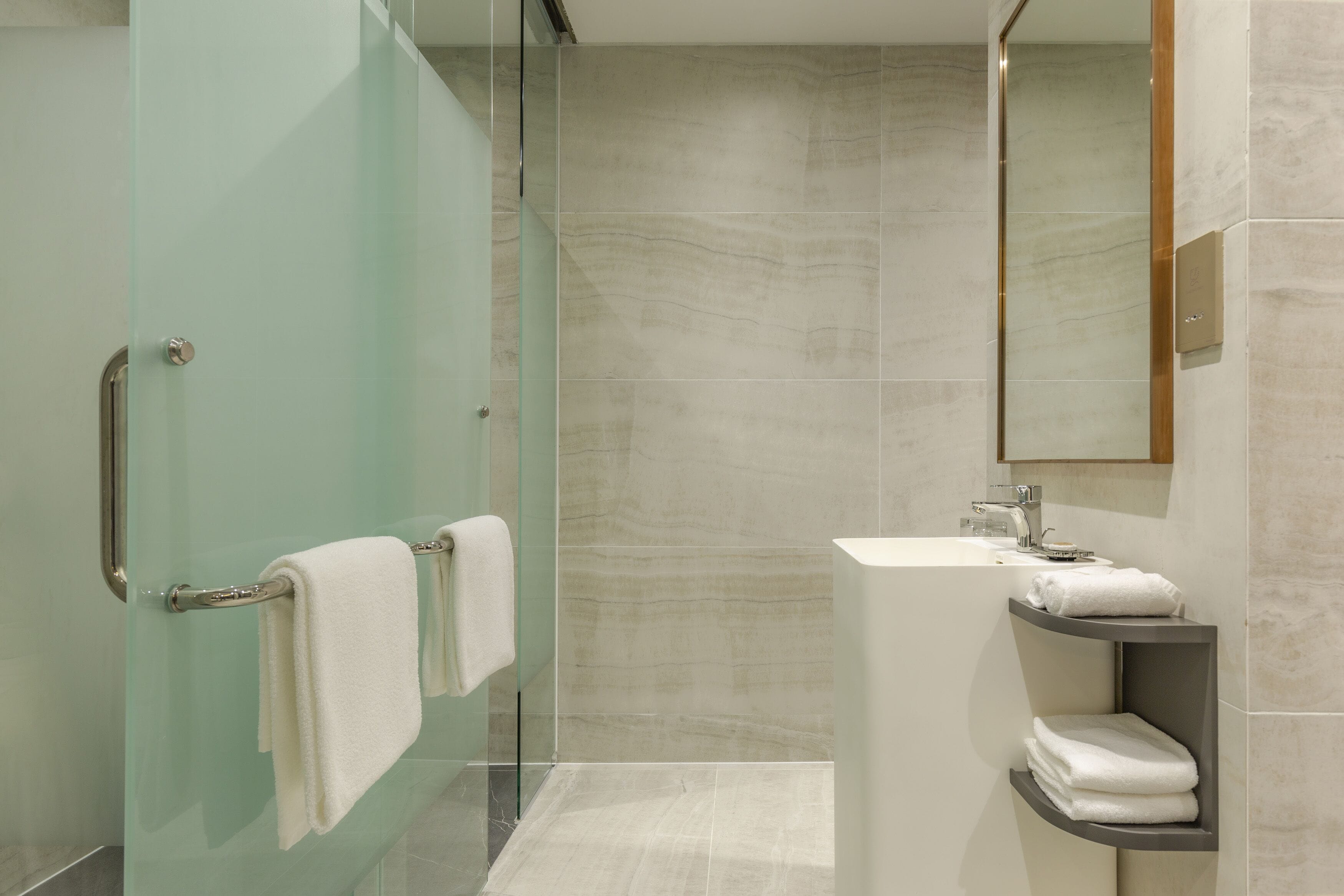 Een moderne badkamer met een glazen douchedeur, een witte wastafel en een spiegel erboven.