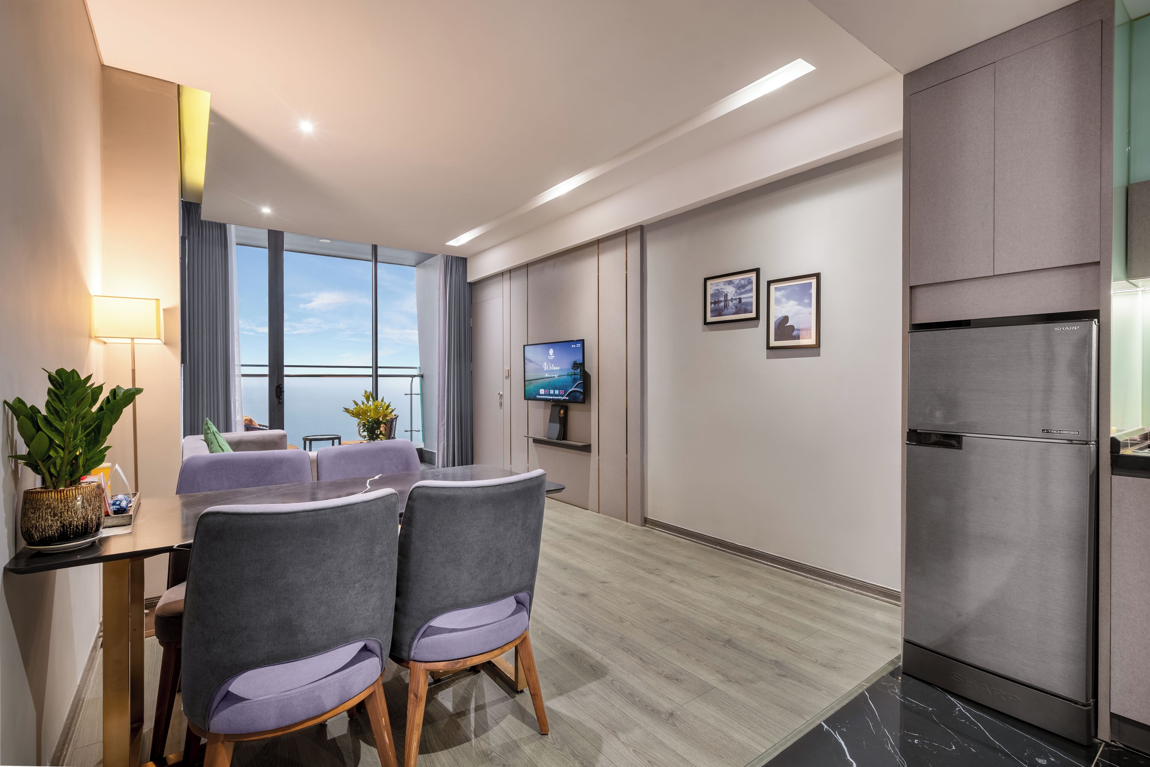 A modern hotel room with a dining area, a TV, and a refrigerator.