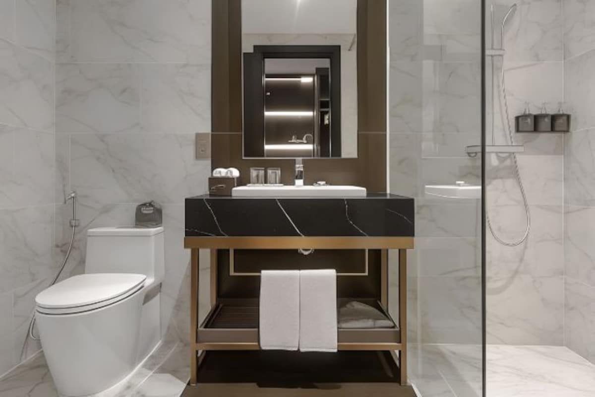 A modern bathroom with a marble vanity, a toilet, and a glass shower enclosure.