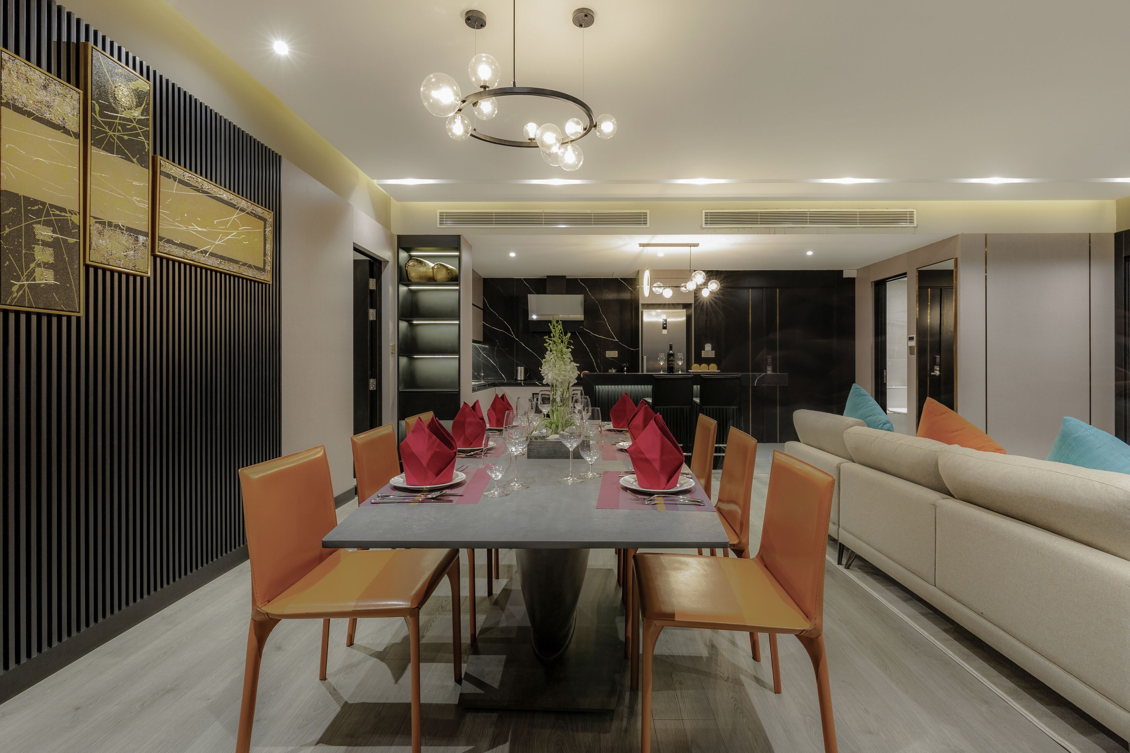 A modern dining room with a long table set for six, surrounded by orange chairs.