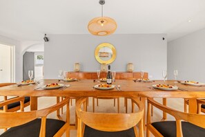 Een eethoek met een grote houten tafel, meerdere stoelen en een kroonluchter in het midden.