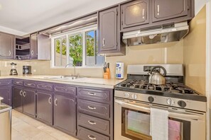 A kitchen with dark cabinets, a gas stove, an oven, a sink, and a window with a view of greenery.