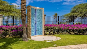 Eine blaue Mosaikwand, eine Palme und rosa Blüten in einem Garten.