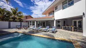 Une maison moderne dotée d’une piscine, de chaises longues et d’un espace repas.