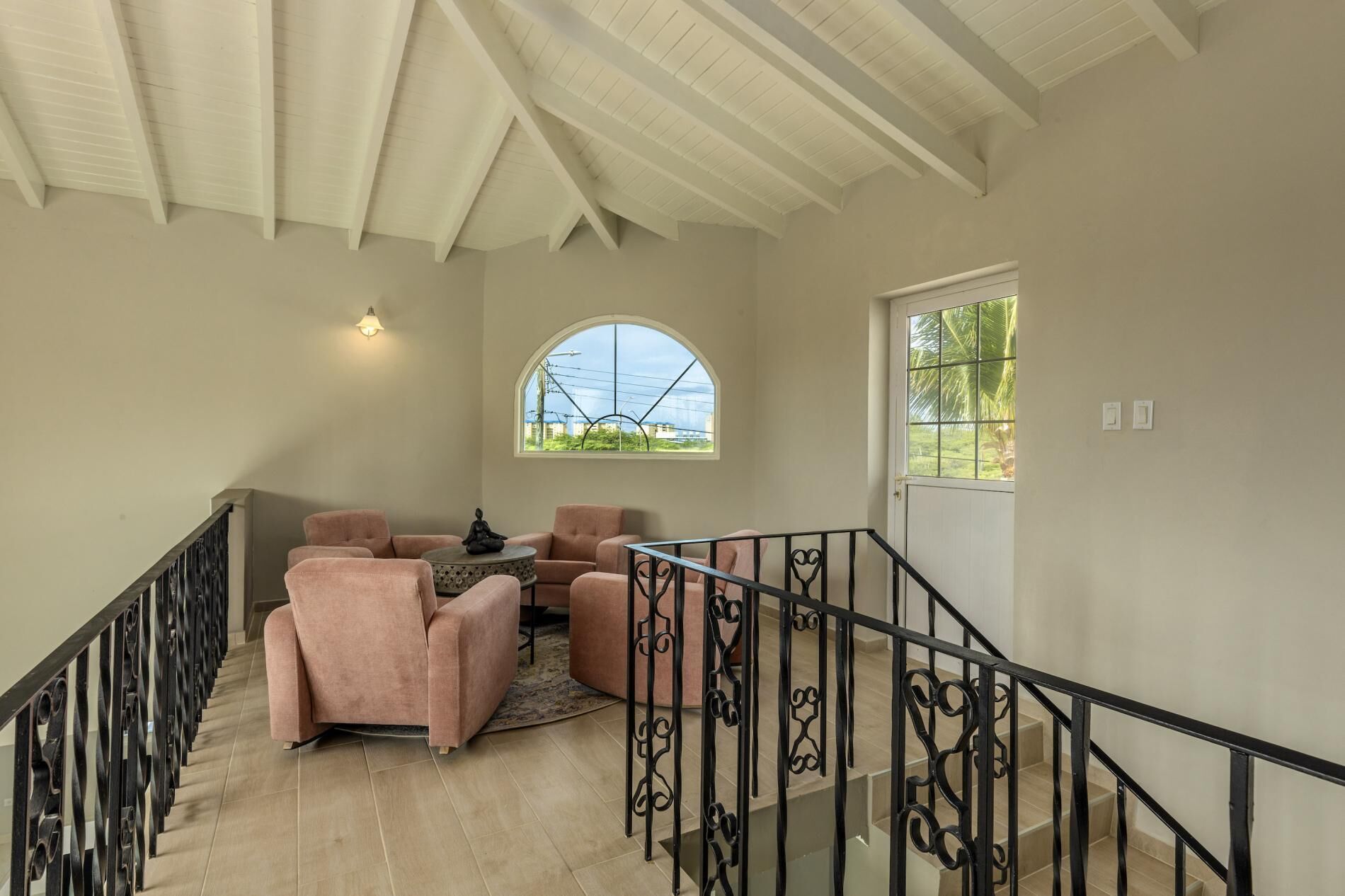 A spacious living area with a high ceiling, a staircase with ornate railings, and large windows offering views of the outdoors.