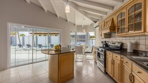 Une cuisine moderne dotée d’un îlot central, de grandes fenêtres et donnant sur un espace piscine.