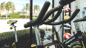 Una hilera de bicicletas estáticas en una sala con ventanas amplias que dan a una zona de piscina.