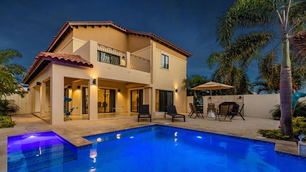 Una casa de dos pisos con piscina, mobiliario exterior y zona de barbacoa.