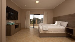 Una habitación de hotel moderna con una cama grande, un televisor montado en la pared y un ventanal corredero que da a un balcón.