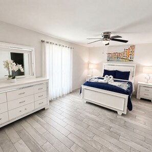 A bedroom with a bed, a nightstand, a dresser, a ceiling fan, and a window with curtains.