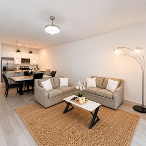A modern living room with a sofa, coffee table, and a dining area with chairs and a kitchen in the background.