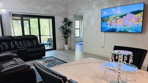 A modern living room with a black leather sofa, a glass coffee table with crystal decorations, and a large TV displaying a nature scene.