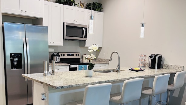 A modern kitchen with a central island, stainless steel appliances, white cabinetry, and a bar area with stools.