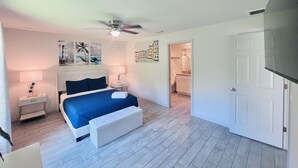 Un dormitorio con cama, mesitas de noche, ventilador de techo y obras de arte en las paredes.