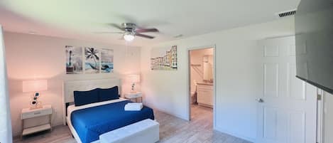 Une chambre à coucher avec un lit, des tables de chevet, un ventilateur de plafond et des œuvres d’art accrochées aux murs.