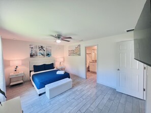 A bedroom with a bed, bedside tables, a ceiling fan, and artwork on the walls.