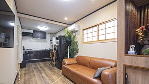 Un espace de vie compact comprenant un coin cuisine, un canapé en cuir marron et un meuble en bois.