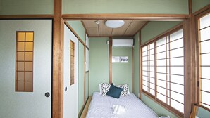 Une pièce de style japonais traditionnel, avec un sol recouvert de tatamis, un lit avec une literie blanche et un oreiller foncé, une porte en bois et de grandes fenêtres à carreaux.
