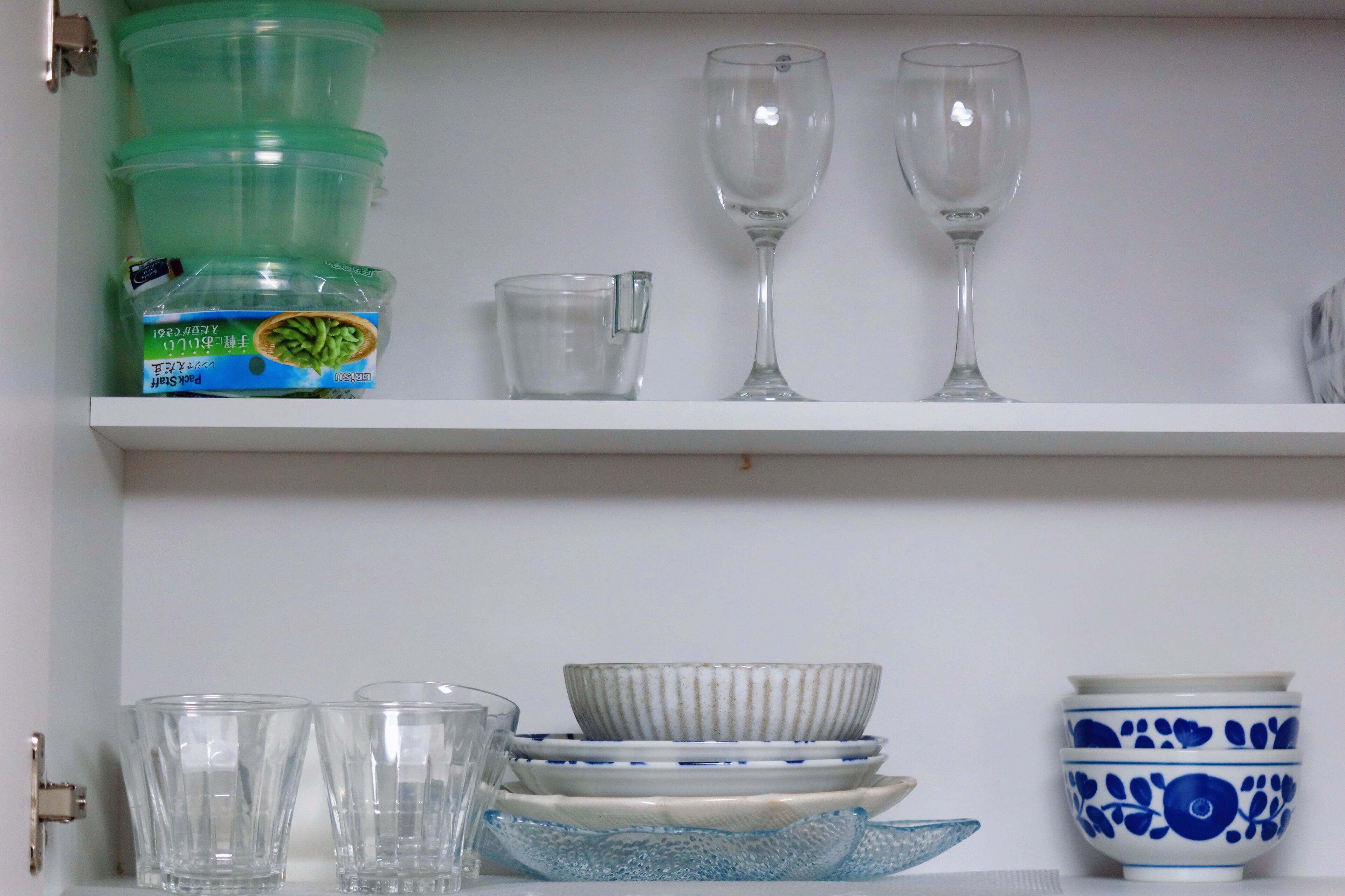 A shelf with various glassware and dishes, including clear glasses, a green container, and blue and white patterned bowls.