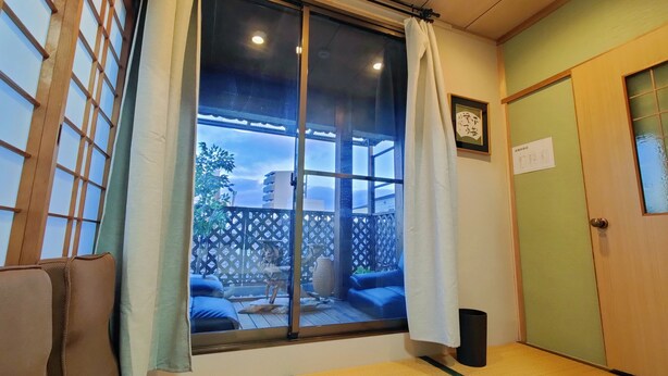 Une pièce avec un sol recouvert de tatamis, une porte coulissante, une vue sur une terrasse extérieure et une petite poubelle.