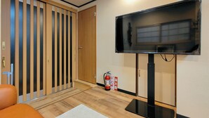 Une pièce avec un téléviseur fixé au mur, une porte en bois à lattes verticales, un extincteur et un tapis blanc sur le sol.