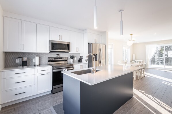 A modern kitchen with white cabinetry, stainless steel appliances, and a large island with a sink.