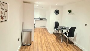 Een moderne keuken met witte kastjes en een roestvrijstalen koelkast. Er is een eethoek met een zwarte tafel en stoelen.