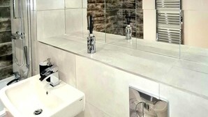 Een moderne badkamer met een grote spiegel, een douche, een wastafel en een handdoekhouder.