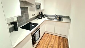 Een moderne keuken met witte kasten, een roestvrijstalen magnetron, een zwart inductiekookplaat en een inbouwoven.
