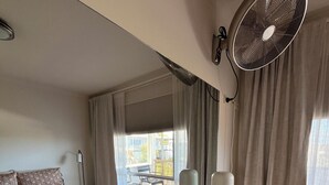 Una habitación de hotel con cama, mesita de noche, lámpara y un ventanal con cortinas.