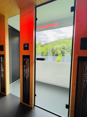 An elevator interior with a control panel, a view of a green landscape through a glass door, and a ceiling with a textured finish.