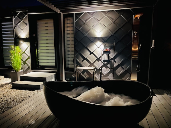 A modern bathroom with a black bathtub, a shower area, and a wall with geometric patterns.