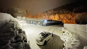 A snowy landscape with a car parked in front of a building with a blue roof, surrounded by snow-covered trees and a fence. - Holiday Home 'Voralpen Lodge - Premium' with Jacuzzi, Terrace & Wi-Fi - Adults Only (Traisen)