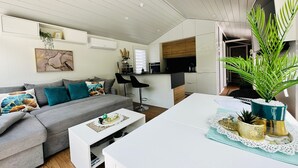 A modern living room with a grey sofa, a white coffee table, and a kitchen area in the background. - Holiday Home 'Voralpen Lodge - Premium' with Jacuzzi, Terrace & Wi-Fi - Adults Only (Traisen)
