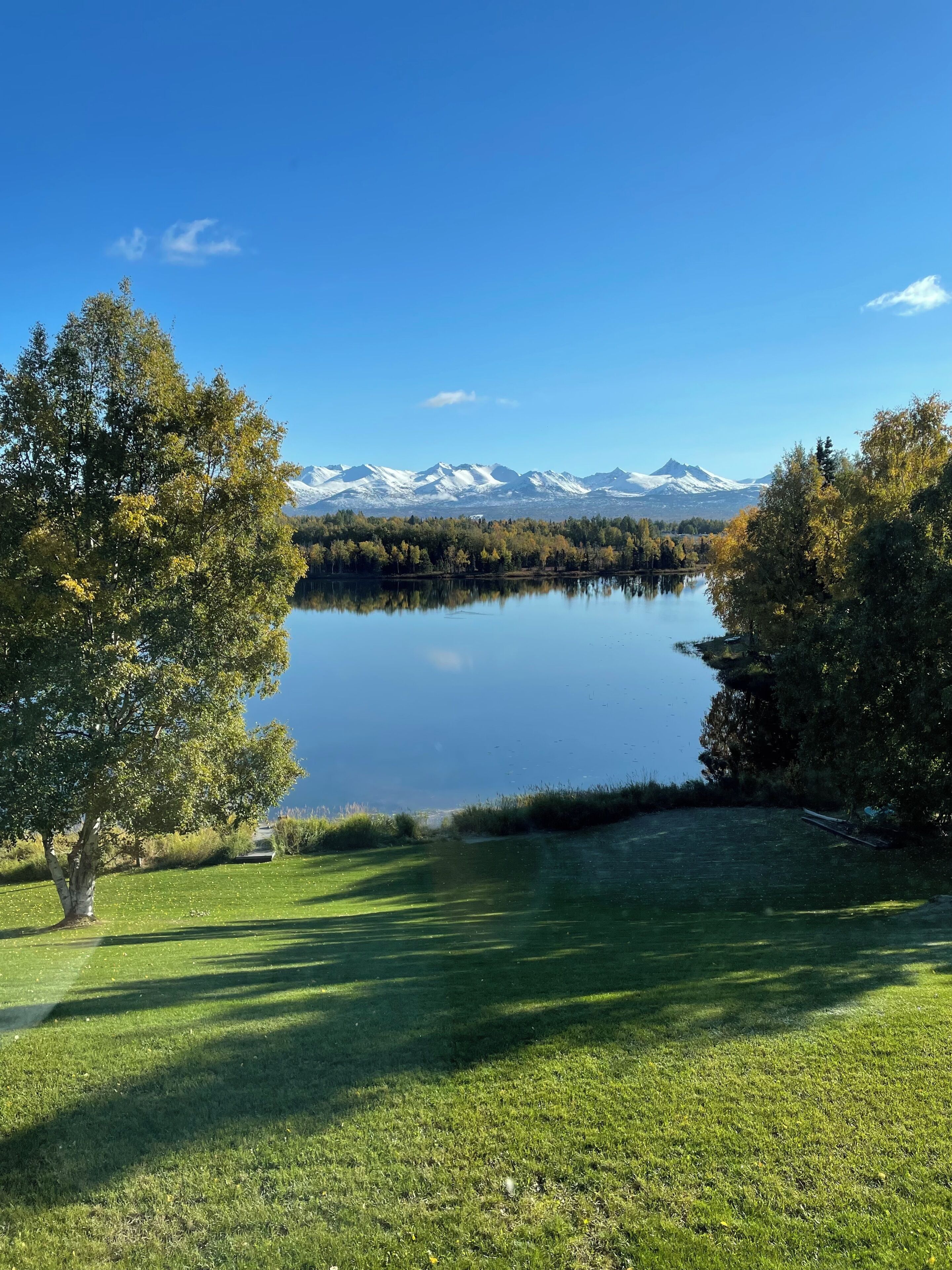 A lake with mountains in the background, surrounded by trees and grass.