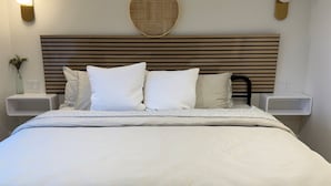 A neatly made bed with a white bedspread, two bedside tables with lamps, and a wall-mounted round mirror.