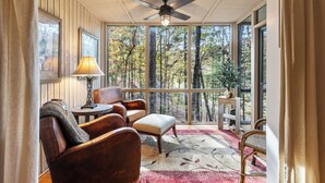 A cozy room with a ceiling fan, large windows, a wooden wall, a table with a lamp, and comfortable seating. - Hiking Trails, Wood-Burning Fireplace & Community Pools - Buckanoe Condo (Jasper)