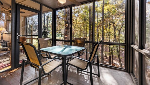 A dining area with a glass table and chairs, large windows with a forest view, and a ceiling fan. - Hiking Trails, Wood-Burning Fireplace & Community Pools - Buckanoe Condo (Jasper)