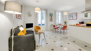 Ein modernes Wohnzimmer mit einer Couch, einem Essbereich mit Tisch und Stühlen, einer Küche mit Herd und einem großen Fenster mit Vorhängen.