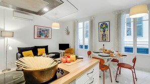 Eine moderne Küche mit einer Holz Arbeitsplatte, einem großen Kochtopf und frischem Gemüse. Es gibt eine Essecke mit Tisch und Stühlen, sowie ein Fenster mit Vorhängen.