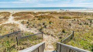 A beach with a wooden boardwalk leading to the water, surrounded by dunes and sparse vegetation. - Beachfront home with beach access, deck, outdoor shower & washer/dryer (Galveston)